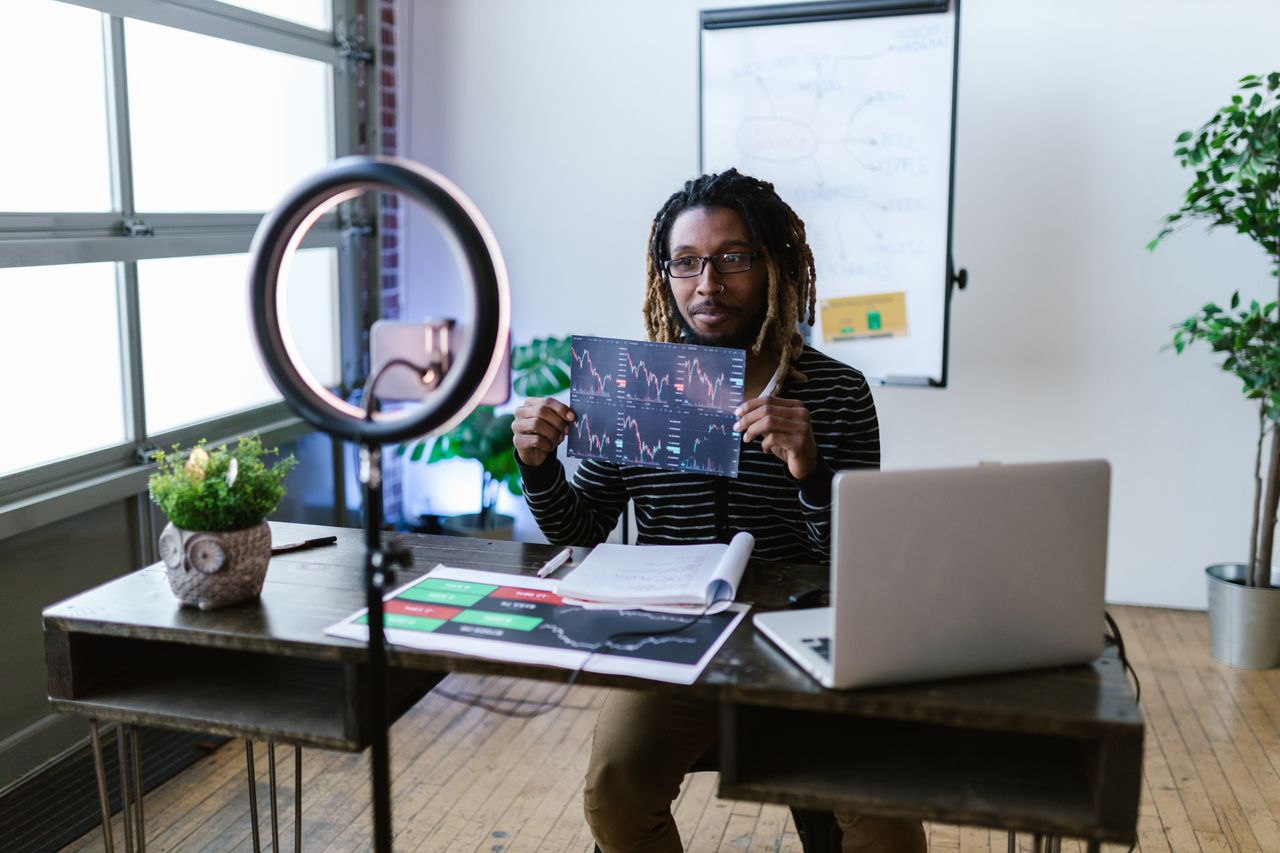 brand-02 A financial vlogger in a home studio discusses cryptocurrency trends using charts and a laptop.