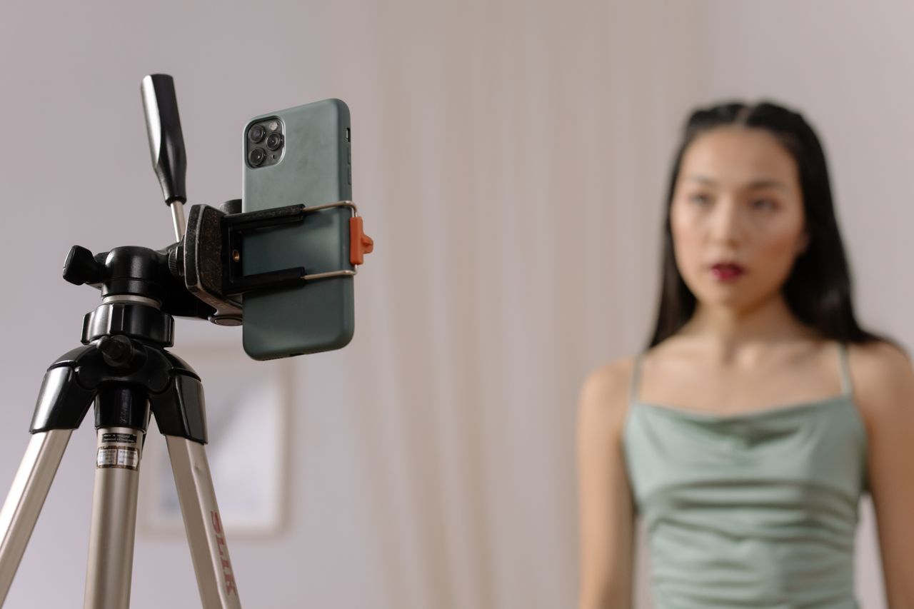 Services-01 A woman stands in front of a smartphone set up on a tripod, engaged in vlogging content indoors.